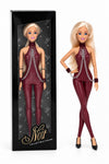 Sammlerpuppe Sweet Restraint Burgundy von Noir Handmade im burgunderfarbenen Catsuit mit Ketten und Handgelenk-Accessoires, neben ihrer Sammlerbox
